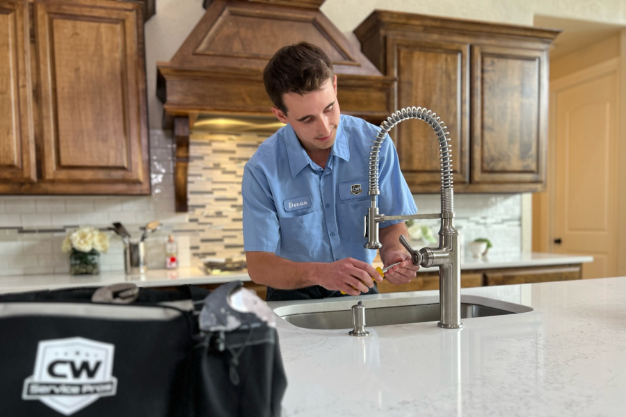 Plumber repairing a leaking kitchen faucet, using tools to tighten loose handle and replace cartridge.