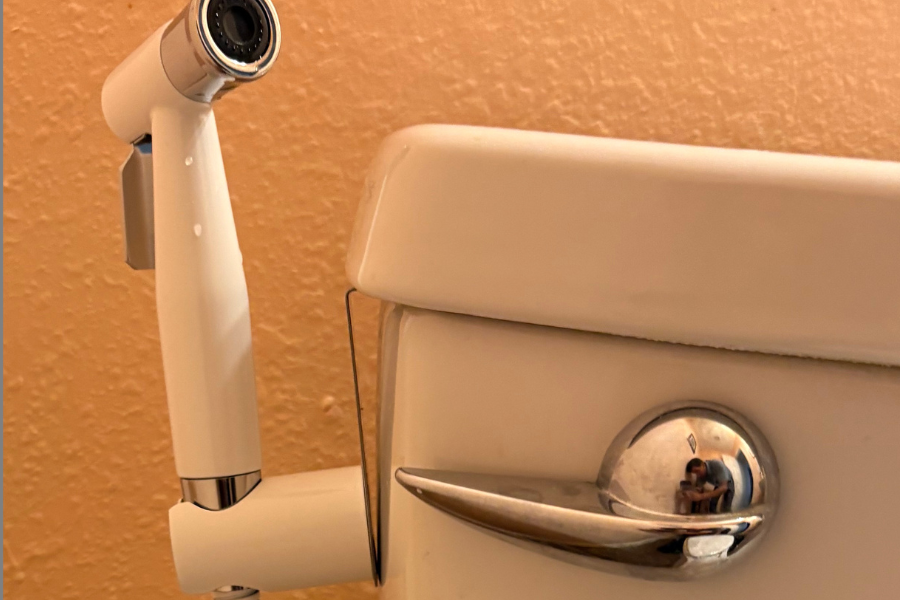 CW Plumber looking at a handheld bidet faucet on a toilet.