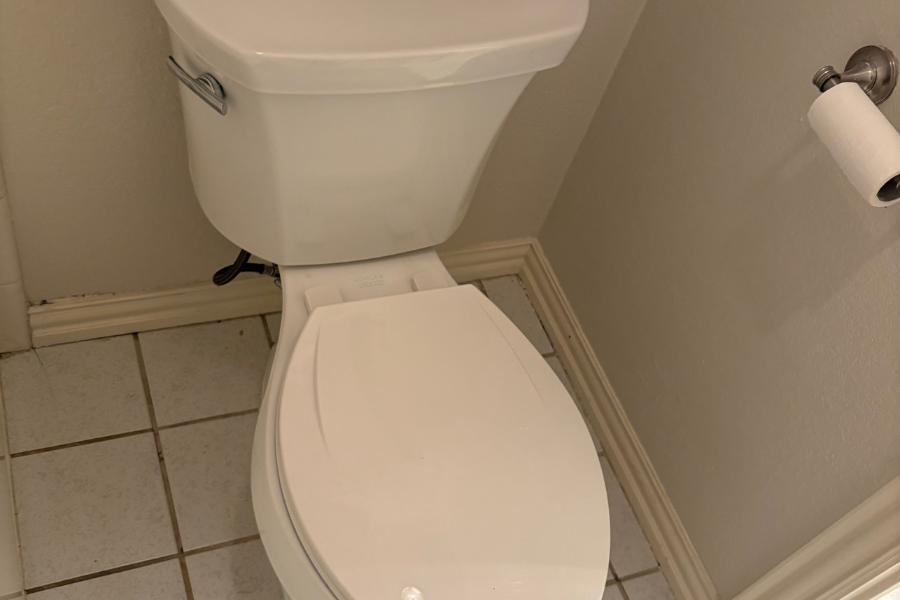 Plumber repairing a white toilet by replacing internal tank components in a residential bathroom.