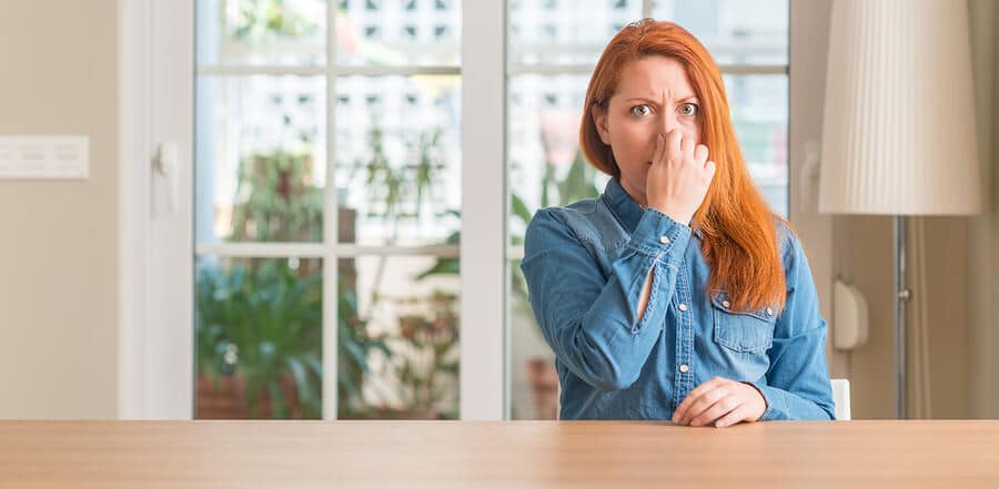Woman covering nose due to unpleasant sewer odor indoors