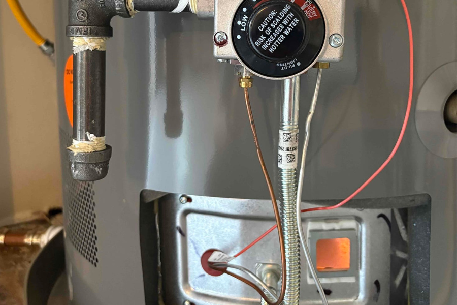 Close-up of a gas water heater’s burner flame, gas supply line, and control valve assembly.
