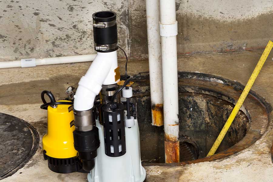 Sump pump installed in basement pit beside drain pipes in The Colony TX