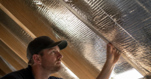 A technician inspecting an attic radiant barrier installed along roof trusses.